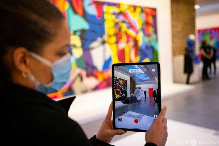 米国人アーティスト、カウズの拡張現実（AR）作品を携帯端末に表示するスタッフ。英ロンドンのサーペンタイン・ギャラリーで（2022年1月18日撮影）。(c)Tolga Akmen : AFP