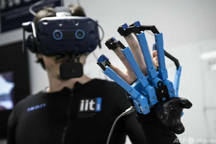 伊ジェノバにあるイタリア技術研究所で、人型ロボット「アイカブ3（iCub 3）」を遠隔操作するための専用スーツと仮想現実（VR）ヘッドセットを装着したオペレーター。手には触覚センサー付きの装置（2022年4月27日撮影）。(c)AFP/MARCO BERTORELLO