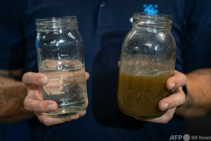 米カリフォルニア州サンフランシスコの集合住宅地下階で、処理済みの排水と未処理の排水を見せる「エピック・クリーンテック」のライアン・プーレイ氏（2023年9月26日撮影）。(c)Loren Elliott / AFP