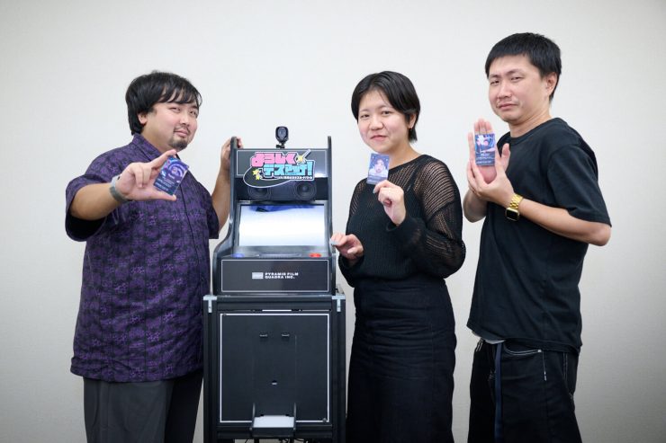 「AI転生ビジネスカードバトル！よろしくデスマッチ！」の筐体と開発メンバーの皆さん