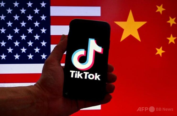 米首都ワシントンで、米中両国の国旗を背景にiPhoneに表示された中国製の動画投稿アプリ「TikTok（ティックトック）」のロゴ（2023年3月16日撮影）。(c)OLIVIER DOULIERY:AFP