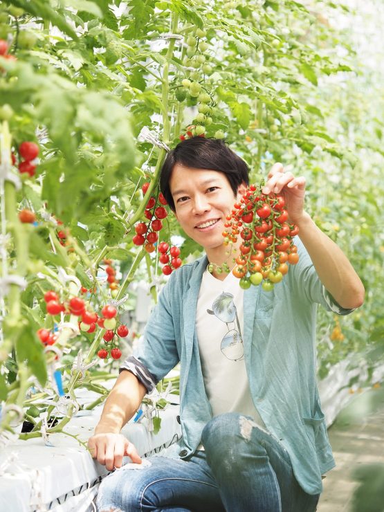 LED植物工場で栽培したミニトマトを持つ矢守氏（写真は温室にて撮影）