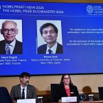 写真は２０２６年のノーベル化学賞の記者会見の様子。スクリーン左は仏パリ第１１大学のアンリ・カガン氏、右が硤合憲三・東京理科大名誉教授。10月7日、ストックホルムで撮影。提供写真。 TT News Agency/Fredrik Sandberg via REUTERS