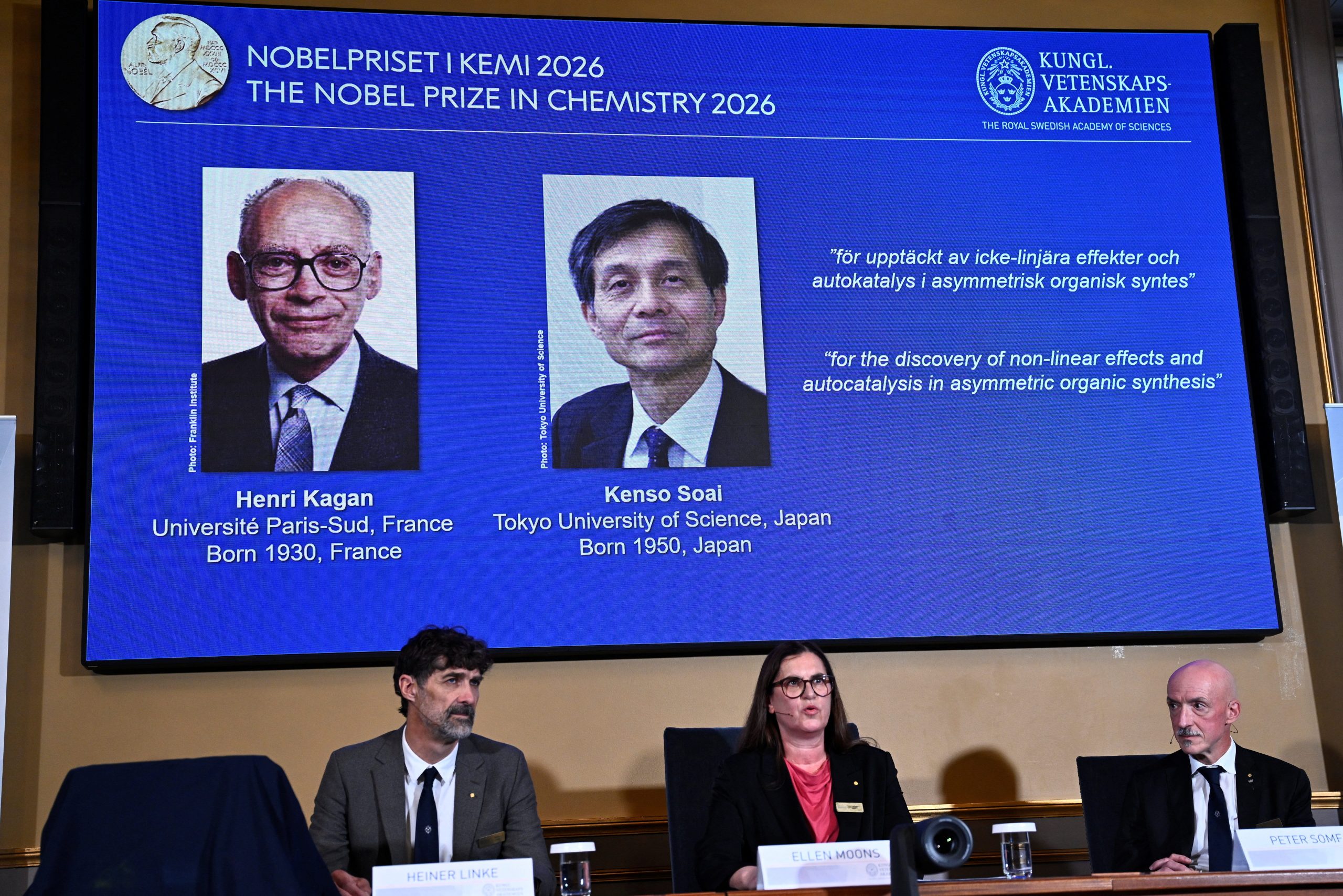 写真は２０２６年のノーベル化学賞の記者会見の様子。スクリーン左は仏パリ第１１大学のアンリ・カガン氏、右が硤合憲三・東京理科大名誉教授。10月7日、ストックホルムで撮影。提供写真。 TT News Agency/Fredrik Sandberg via REUTERS